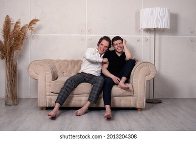 Two Handsome And Lovely Men Are Sitting On The Couch. Best Friends And Leisure Time Together. Watching Serials In Front Of The TV.