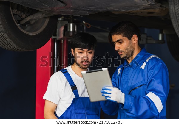 Two handsome male mechanics wearing uniform,\
using tablet, checking or inspecting for fix, repair car or\
automobile components, working in car maintenance service center or\
shop. Industry Concept