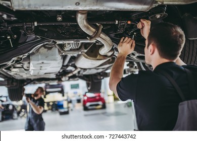 Two handsome mechanics in uniform are working in auto service with lifted vehicle. Car repair and maintenance. - Shutterstock ID 727443742