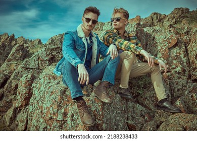 Two Handsome Men In Denim Clothes Pose Outdoor Sitting On The Rocks. Denim Style And Male Fashion. 