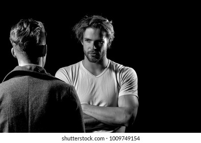 Two handsome men standing with faces opposite on black background. Muscular macho, unshaven caucasian, in white tshirt with folded arms, biceps, triceps. Male businessman in dark coat