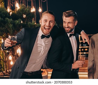 Two handsome men in suits drinking whiskey and smiling while spending time on party - Shutterstock ID 2070300353