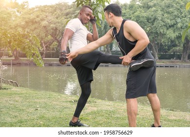 Two handsome muscular men exercising together by  river in  green forest park. Asian trainer is training kicking and punching for  African American boxer. Athletes man stretching and warm-up outdoors.