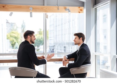 Two handsome young businessmen sitting and talking in office - Shutterstock ID 501282670