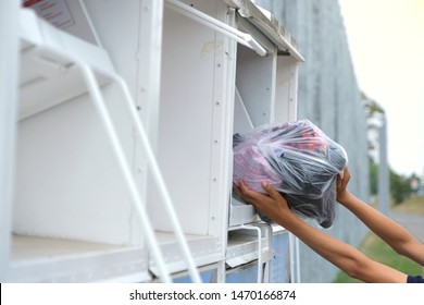 Two Hands(teenage Boy) Putting A Plastic Bag Full Of Colourful Used Clothing  Into Old White Clothes Donation Bins Or Containers For Shoes And Textiles. Recycling And Clothing Bank Outside.