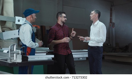 Two Handymen And Foreman Standing And Talking In Joinery Shop.