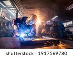 The two handymen performing welding and grinding at their workplace in the workshop, while the sparks "fly" all around them, they wear a protective helmet and equipment.