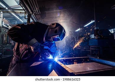 The two handymen performing welding and grinding at their workplace in the workshop, while the sparks "fly" all around them, they wear a protective helmet and equipment.