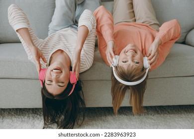 Two happy adult women mature mom young kid wearing casual clothes headphones listening music lying on gray sofa couch stay at home flat rest relax spend free spare time in living room. Family concept - Powered by Shutterstock