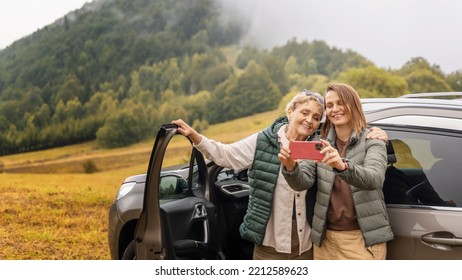 Two happy adult women mother and daughter traveling together by car taking selfie standing next to the car - Shutterstock ID 2212589623