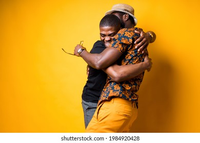 Two happy African American friends hug and laugh after a long time apart. Isolated on yellow background