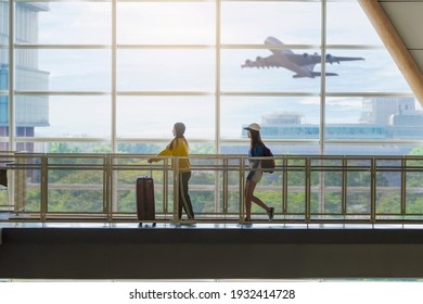Two happy Asian girls traveling abroad together, carrying suitcase luggage and running through big window of airport while airplane fly in airport.  - Shutterstock ID 1932414728