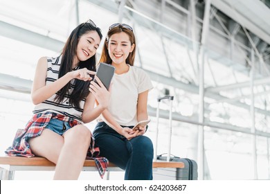 Two Happy Asian Girls Using Smartphone Checking Flight Or Online Check-in At Airport Together, With Luggage. Air Travel, Summer Holiday, Or Mobile Phone Application Technology Concept