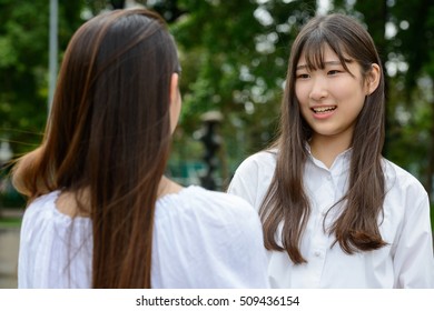 Two Happy Asian Woman Friends Talking With Each Other Outdoors In Park