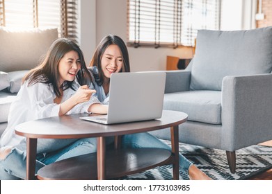 Two Happy Asian Women Best Friends In Casual Wear Laughing While Working With Laptop At Home In Living Room