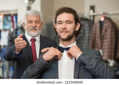 Two Happy Atractive Elegant Men Choosing Clothes For Special Occaision. Older Man With Grey Hair Helping His Brunette Son With Shopping. Customer With Cutly Hair Fitting New Look With Bow Tie.