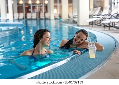 Two happy attractive brunette female friends in bikini enjoys and relax in hotel indoor swimming pool.