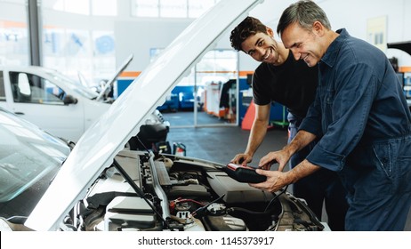 Two Happy Automobile Mechanics Doing Car Engine Checkup With A Device. Mechanics Diagnosing A Car In Service Station.