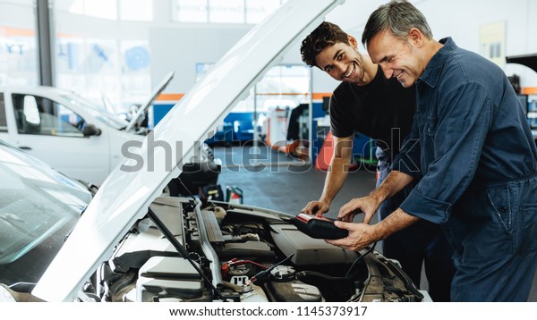 Two happy\
automobile mechanics doing car engine checkup with a device.\
Mechanics diagnosing a car in service\
station.