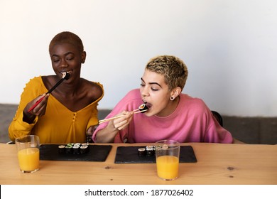 Two happy beautiful female couple eating vegan sushi rolls while sitting at home