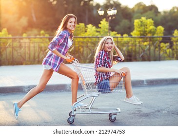 Two Happy Beautiful Teen Girls Driving Shopping Cart Outdoors, Lifestyle Concept