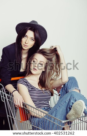 Two happy beautiful teen girls driving shopping cart indoors, lifestyle concept