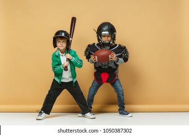 Two Happy Boys Showing Different Sport. Studio Fashion Concept. Emotions Concept. Boys Likes Sport. American Football And Baseball. Children's Fashion Show. Sport Style. Teen And Kids Fashion Concept.