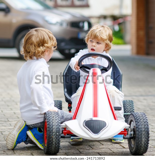 Two happy brothers boys playing with toy car in\
summer garden, outdoors. Kids having fun in domestic garden or\
nursery on sunny warm day.