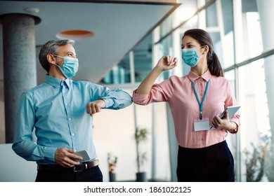 Two happy business coworkers elbow bumping and wearing protective face masks in a hallway of an office building.  - Powered by Shutterstock