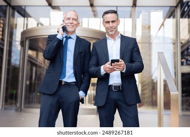 Two happy businessmen standing outside office building talking on a smartphone - Powered by Shutterstock