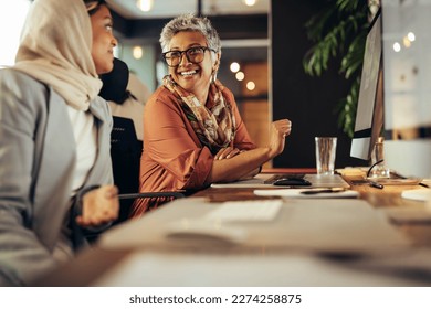 Two happy businesswomen having a discussion while working at their desks in an office. Diverse businesswomen working as a team in a creative co-working office.