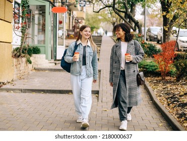 Two happy carefree multiracial girlfriends walking city street with take away coffee, talking and sharing life stories, multiethnic female best friends enjoying autumn walk outdoors. Womens friendship - Powered by Shutterstock