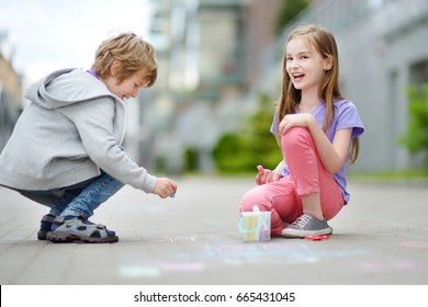 Two Happy Children Drawing With Colorful Chalks On A Sidewalk. Summer Activity For Small Kids. Creative Leisure For Family. 