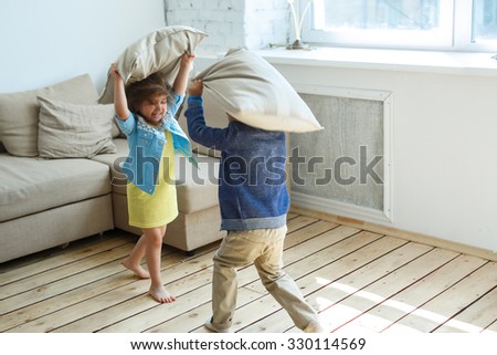 Two happy children is fighting a pillows each other at home