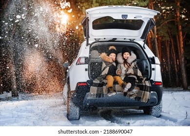 Two Happy Children On Walk In Winter Forest. Children Sit In Trunk Of Family Car. Children Warm Themselves Wrapped In A Warm Blanket.