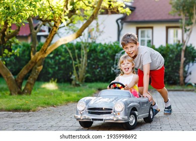 Zwei glückliche Kinder, die mit einem großen alten Spielzeugauto im Sommergarten spielen, draußen. Ein kleiner Junge, der Auto schiebt und fährt mit einem kleinen kleinen Mädchen, süße Schwester drinnen. Kinder lachen und lachen. Schöne Familie