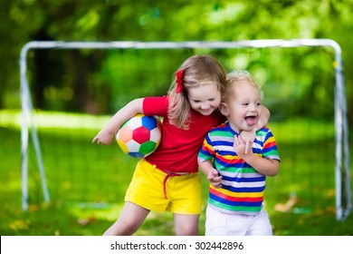 Two Happy Children Playing European Football Outdoors In School Yard. Kids Play Soccer. Active Sport For Preschool Child. Ball Game For Young Kid Team. Boy And Girl Score A Goal In Football Match.