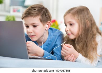 Two happy children playing with laptop and listening music with headphones in bed - Powered by Shutterstock