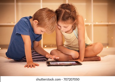 Two happy children playing on the tablet in the kids room at home, best friends with pleasure spending time together, smart kids using smart technology