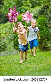 Two Happy Children Running In Garden In Summer With Windmills