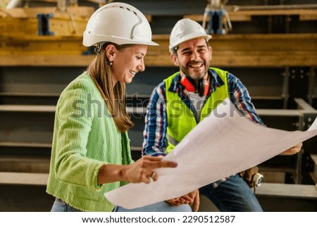 Two happy civil engineer and maintenance engineer in protective vests and helmets working on a construction site