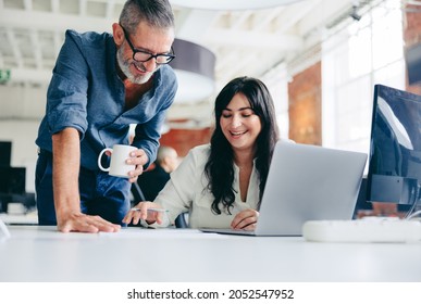 Two happy colleagues collaborating on a new project in the office. Mature businessman teaming up with his female colleague in a modern office. Two colleagues smiling while working together. - Shutterstock ID 2052547952