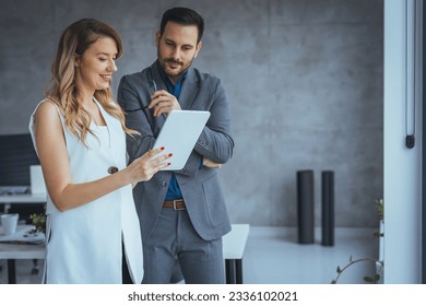 Two happy colleagues smiling cheerfully in an office. Happy mature businessman holding a smartphone while standing with his female colleague in a modern workplace. Businesspeople working as a team. - Powered by Shutterstock