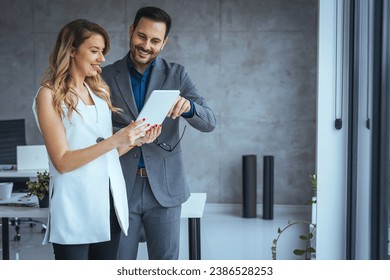 Two happy colleagues smiling cheerfully in an office. Happy mature businessman holding a smartphone while standing with his female colleague in a modern workplace. Businesspeople working as a team. - Powered by Shutterstock