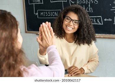 Two happy college students girls giving high five in classroom. Young laughing cheerful African American and latin women classmates team celebrating successful teamwork result in office with highfive.