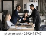 Two happy confident business partners men shaking hands over large table, meeting with project colleagues, managers, closing deal, contract, discussing investment to startup, partnership
