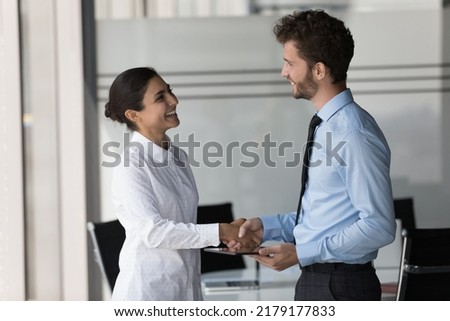 Two happy confident diverse business people shaking hands in office, smiling, laughing, talking. Customer giving handshake to manager, lawyer, ending meeting, negotiation, deal