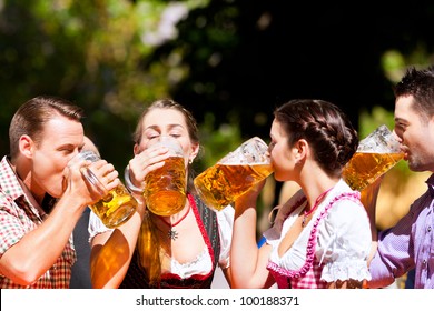 Two Happy Couples Sitting In Bavarian Beer Garden And Enjoy The Beer And The Sun