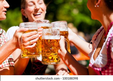 Two Happy Couples Sitting In Bavarian Beer Garden And Enjoy The Beer And The Sun