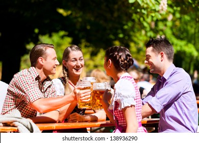 Two Happy Couples Sitting In Bavarian Beer Garden And Enjoy The Beer And The Sun